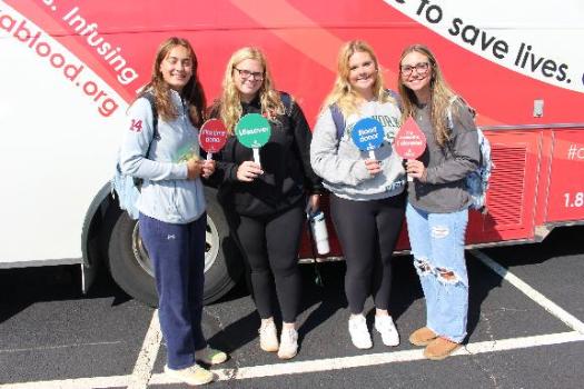 Four blood donors in front of the mobile donor bus at the Goldey-Beacom College Blood Drive .